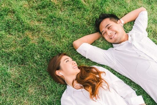 Young man and woman happily lying on the grass with headsets. 