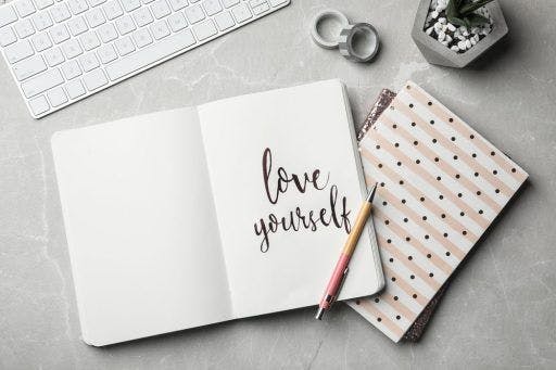 Flat lay of open notebook with calligraphy that says “love yourself.”