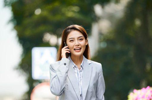 Smiling businesswoman in grey on the phone while walking outdoors.