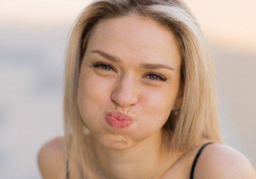 Blonde woman puffing up face while smiling.