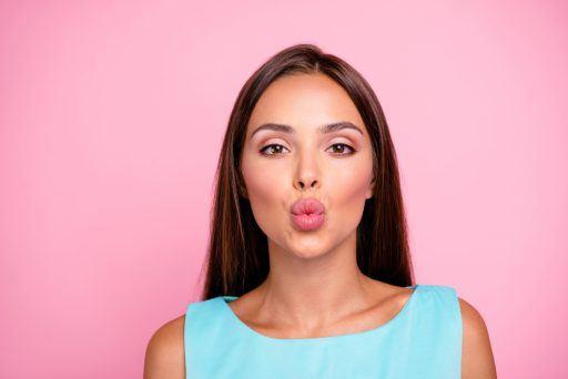 Brunette making a kissy face against pink background.