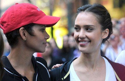 Halle Berry in a red cap and Jessica Alba smiling at each other at a public event.
