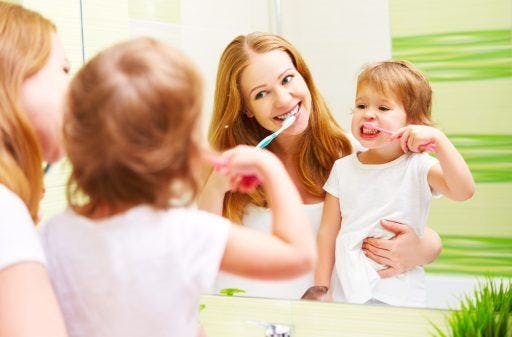 Mother and daughter happily brushing teeth in front of a mirror.