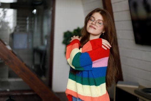 Woman in rainbow sweater hugging herself.