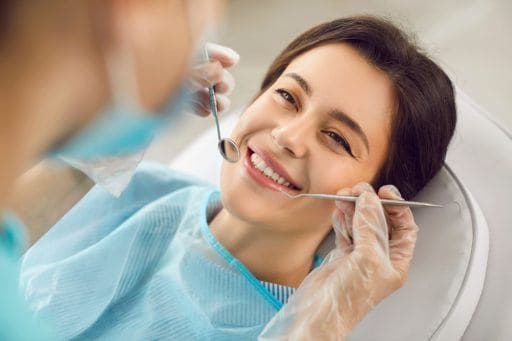 Woman lying on dentist’s chair smiling as dentist brings tools near her mouth.